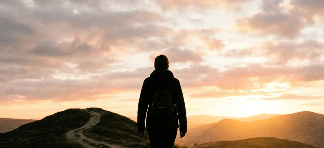 Person walking on a mountain path with a dark cloud above their head at sunset
